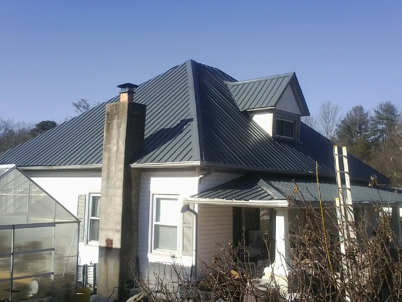 Dark blue standing seam metal roof on a white farmhouse with dormer — Slate & Tile Roof Repair by Roofing Brothers in Saylorsburg