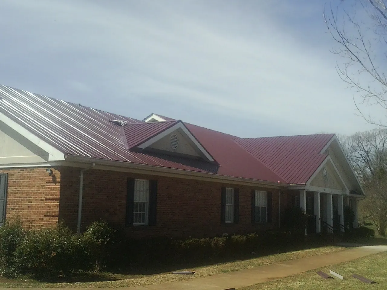 Red metal roof with gabled entries on a long brick building, from a Hail Damage Roof Repair job in Saylorsburg