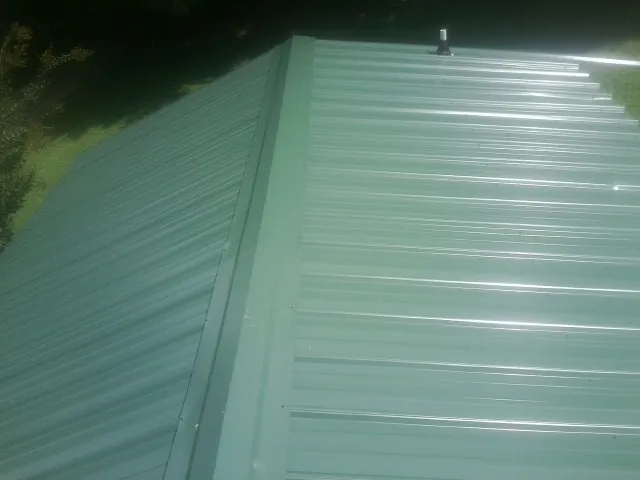 New green metal panels meeting at the ridge of a roof — Flat Roof Repair work by our crew in Saylorsburg