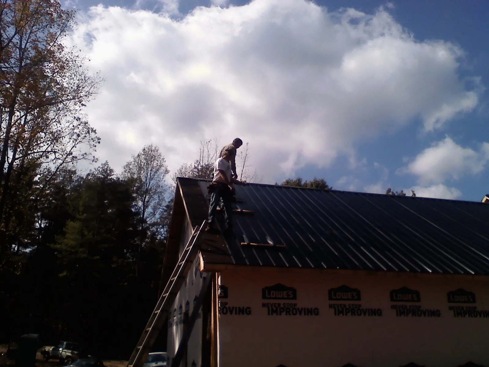 Roofer fastening dark metal panels high against a cloudy sky, from a Roof Inspection job in Saylorsburg