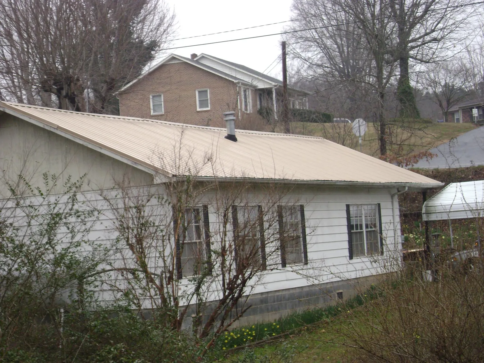 Tan metal roof on a white sided house set into a hillside — Commercial Roofing by Roofing Brothers in Saylorsburg